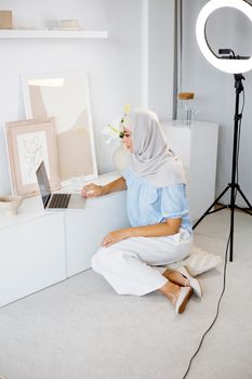 Woman in hijab working on laptop in modern home office with ring light setup.