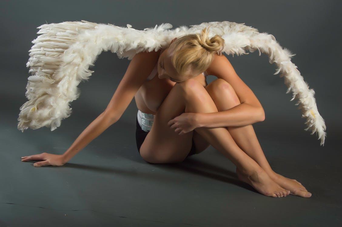 Woman Wearing White Angel Wings Sitting on Ground While Leaning Her Head on Her Knees