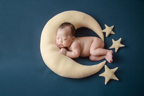 A Newborn Baby Sleeping while Lying on a Moon Shaped Pillow