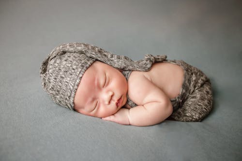 A Newborn Baby in Gray Knitted Cap Lying Down while Sleeping