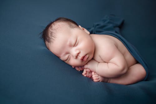 A Newborn Baby Covered in Blue Blanket while Sleeping