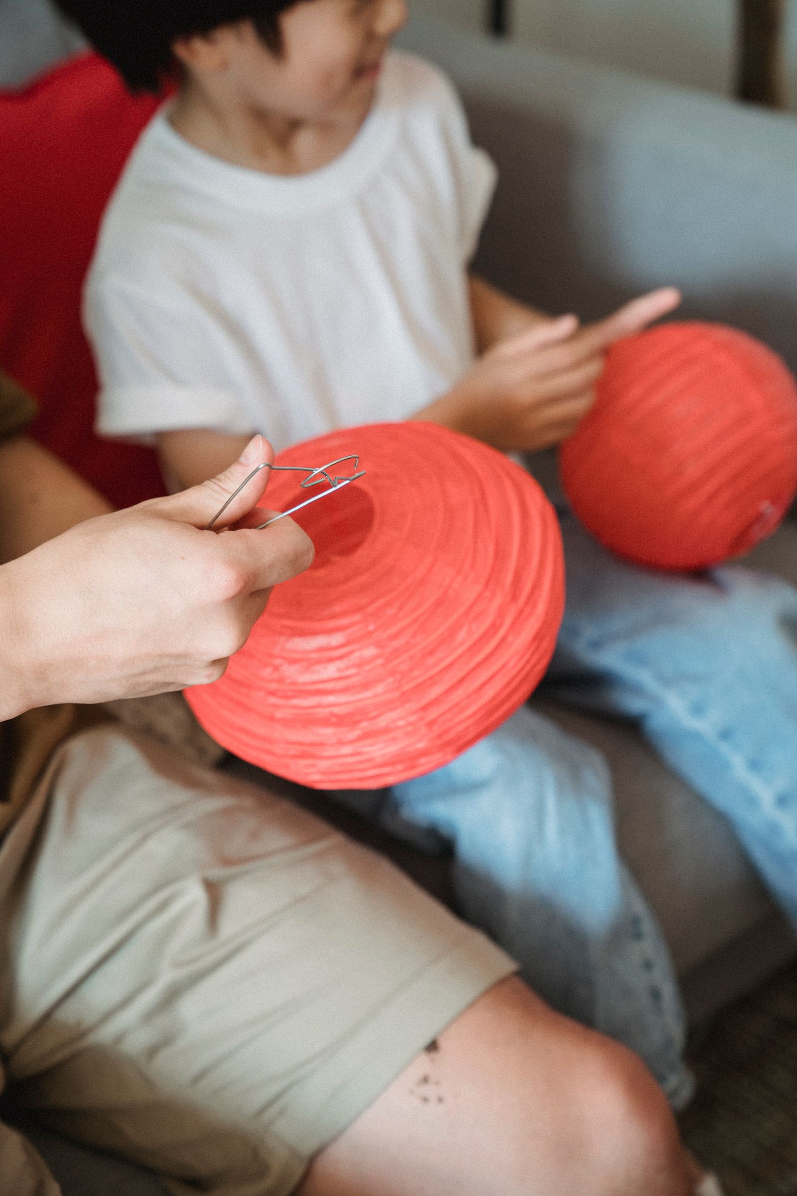 Family hands assembling red paper lanterns indoors. Photo: Kevin Malik / Pexels.