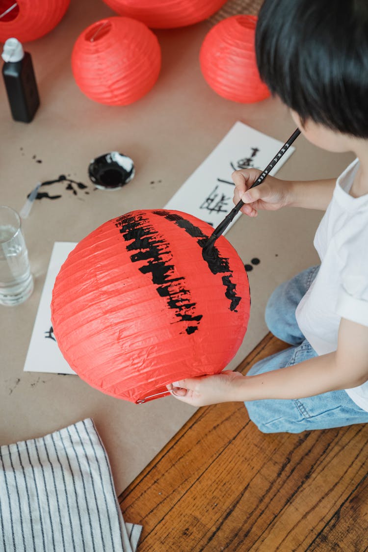 A Child Holding A Red Lantern While Painting