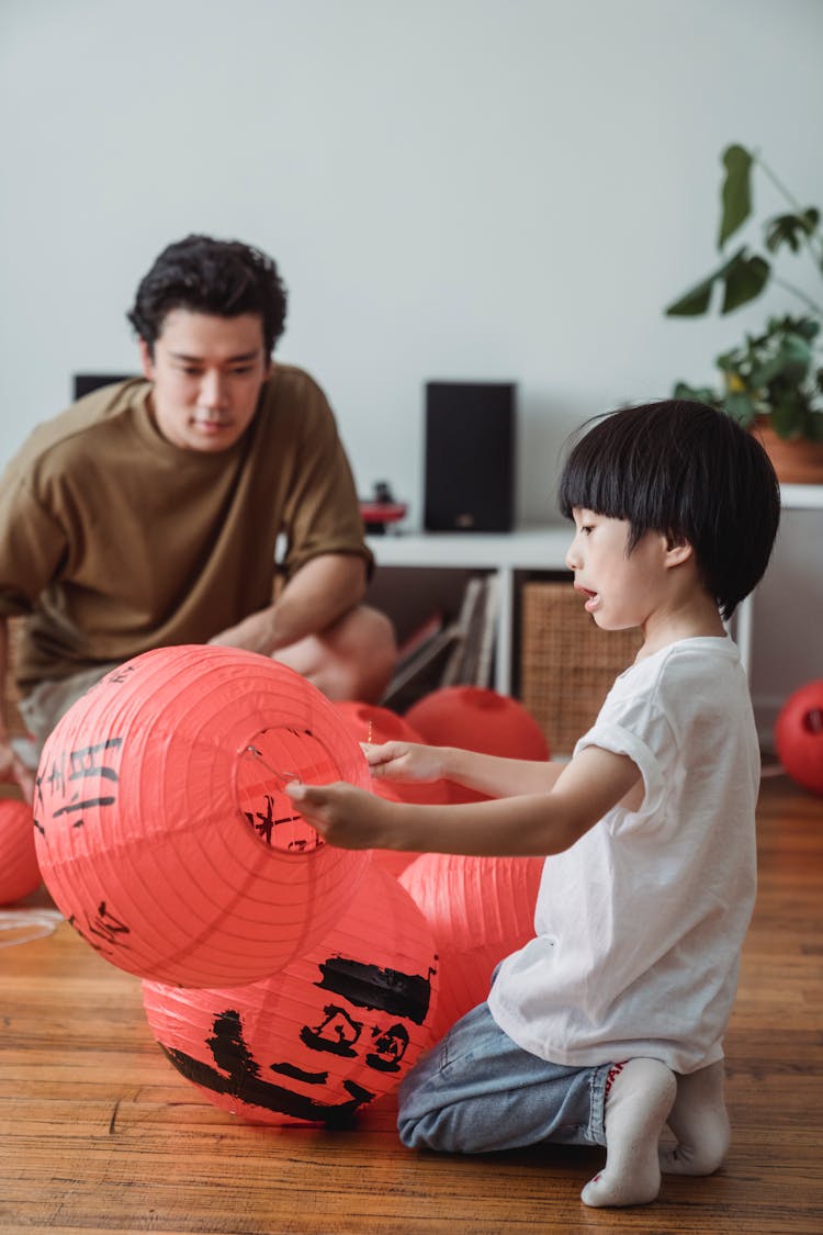 A Boy Kneeling On Wooden Floor Holding A Chinese Lantern