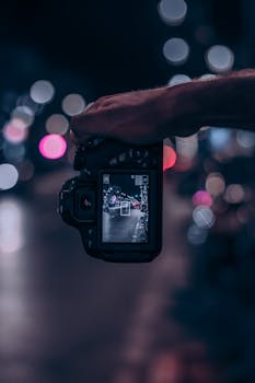 Close-up of a DSLR capturing a city street at night, highlighting bokeh lights.