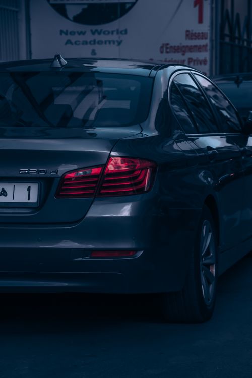 Free Elegant gray luxury sedan with visible tail lights parked on an urban street at night. Stock Photo
