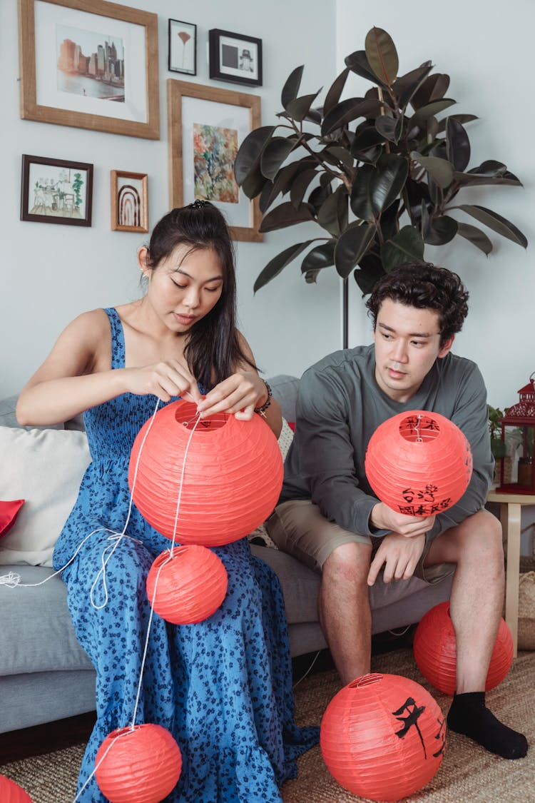 A Man And Woman Sitting On The Couch While Holding Red Lanterns