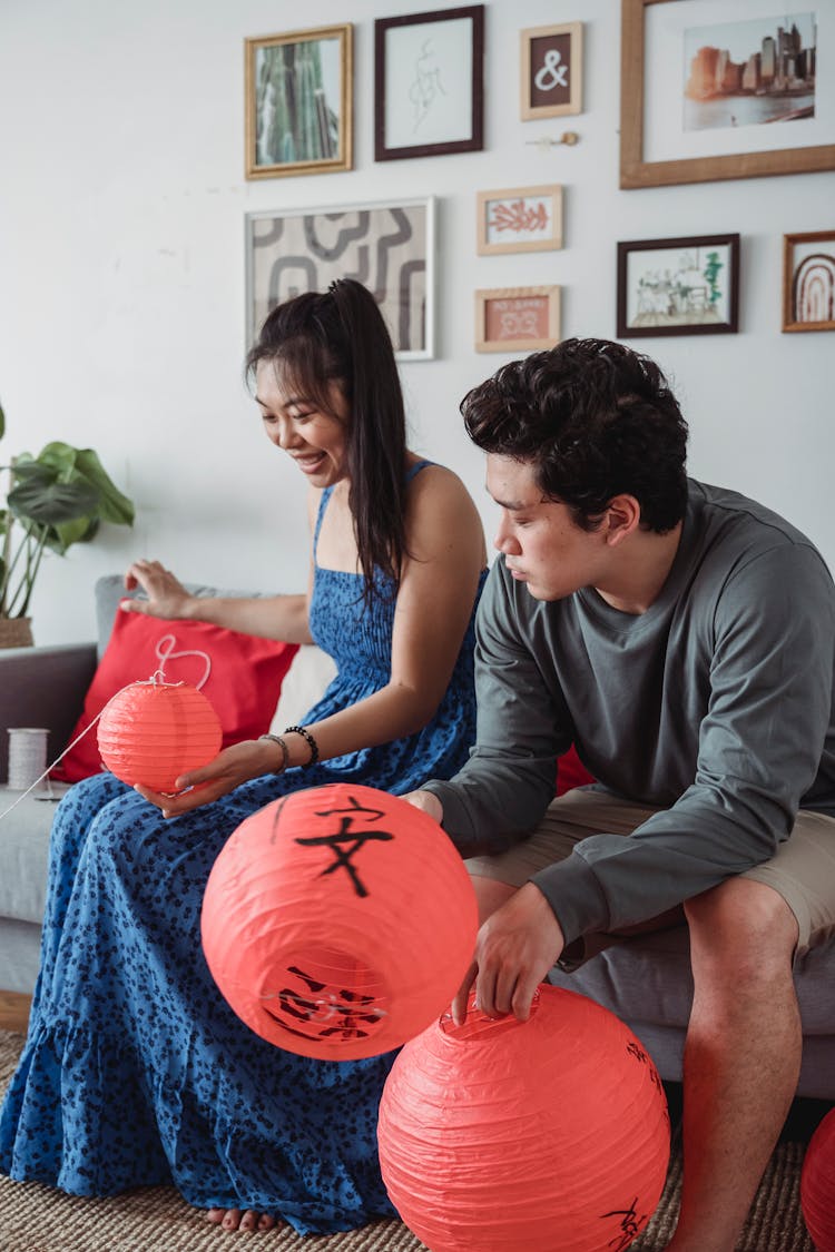 A Husband And Wife Holding Chinese Lanterns While Sitting On The Couch