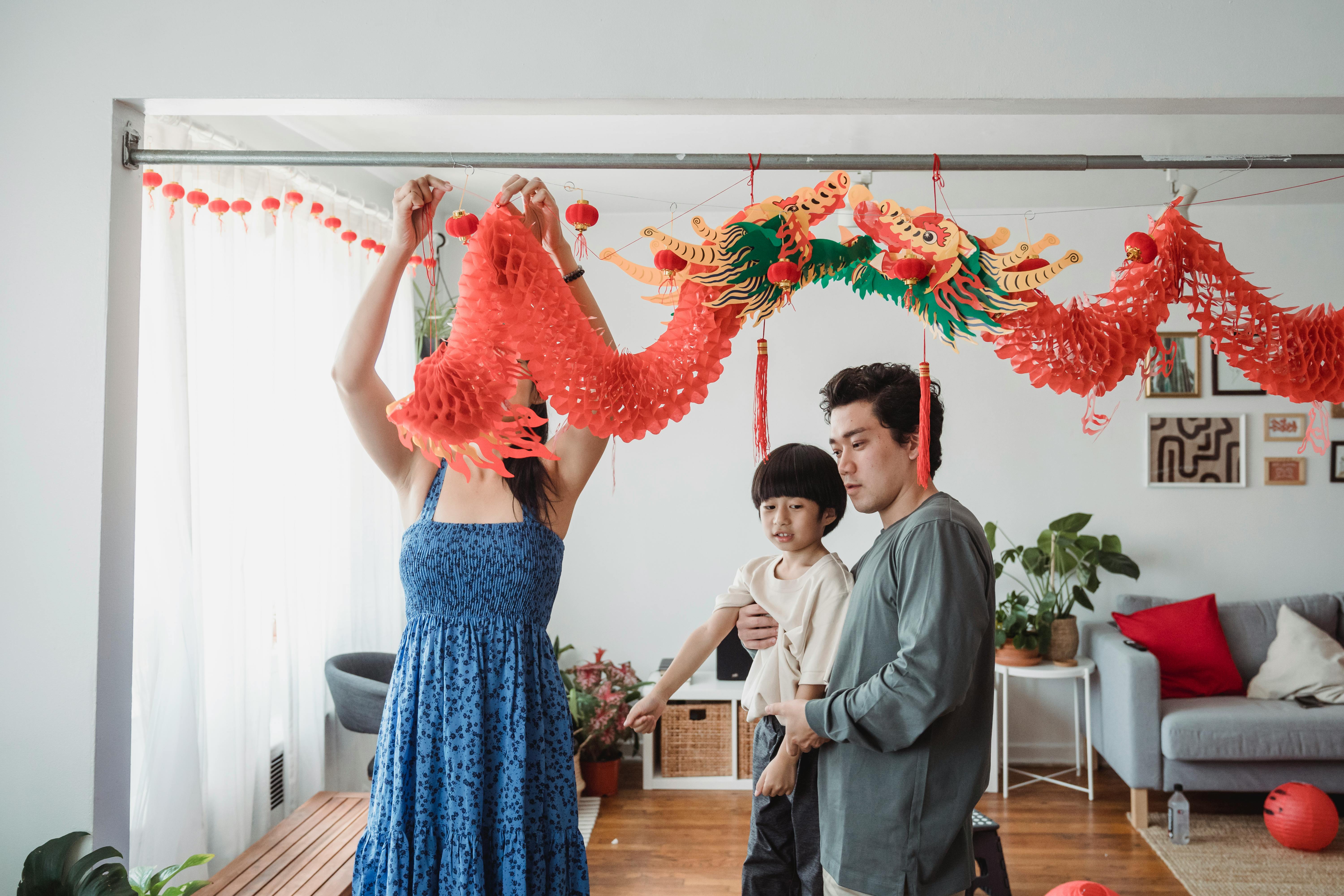 man in gray shirt carrying child next to a woman hanging decorations