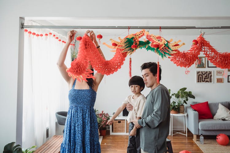 Man In Gray Shirt Carrying Child Next To A Woman Hanging Decorations