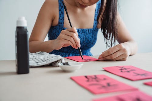 A Woman in Blue Tank Top Writing on Red Paper