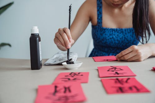 Woman in Blue Sleeveless Top Holding Paint Brush and Writing on Pink Paper