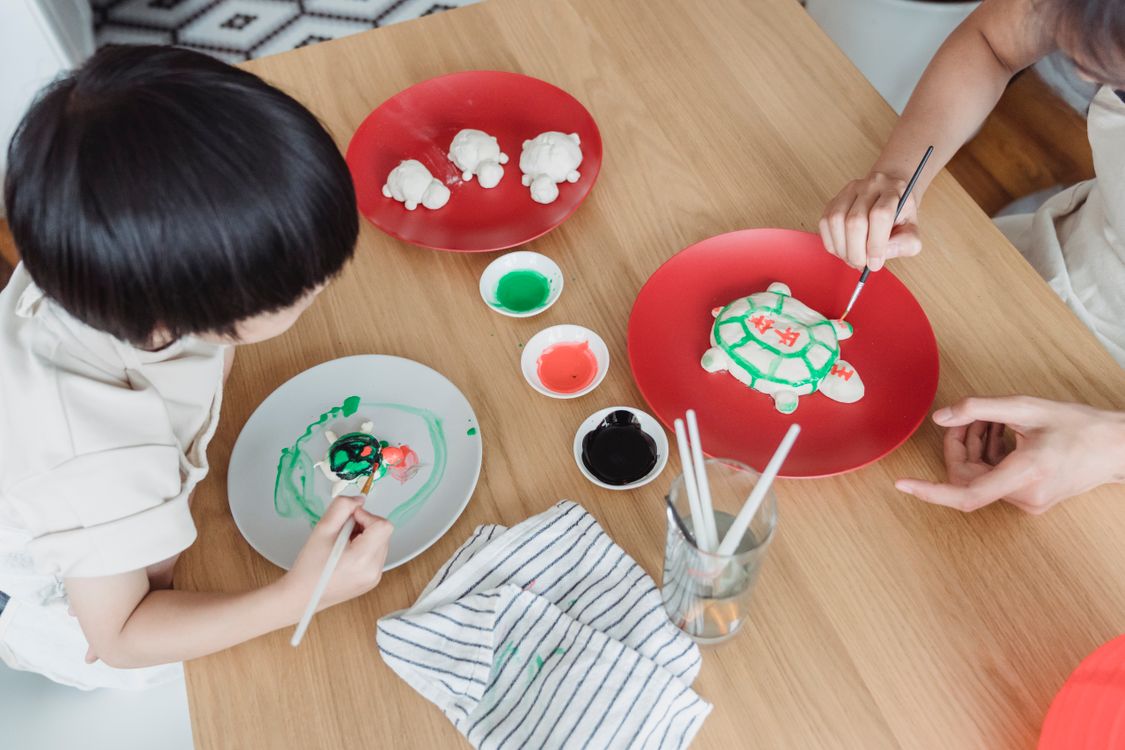 Een ouder en kind schilderen samen aan een houten tafel