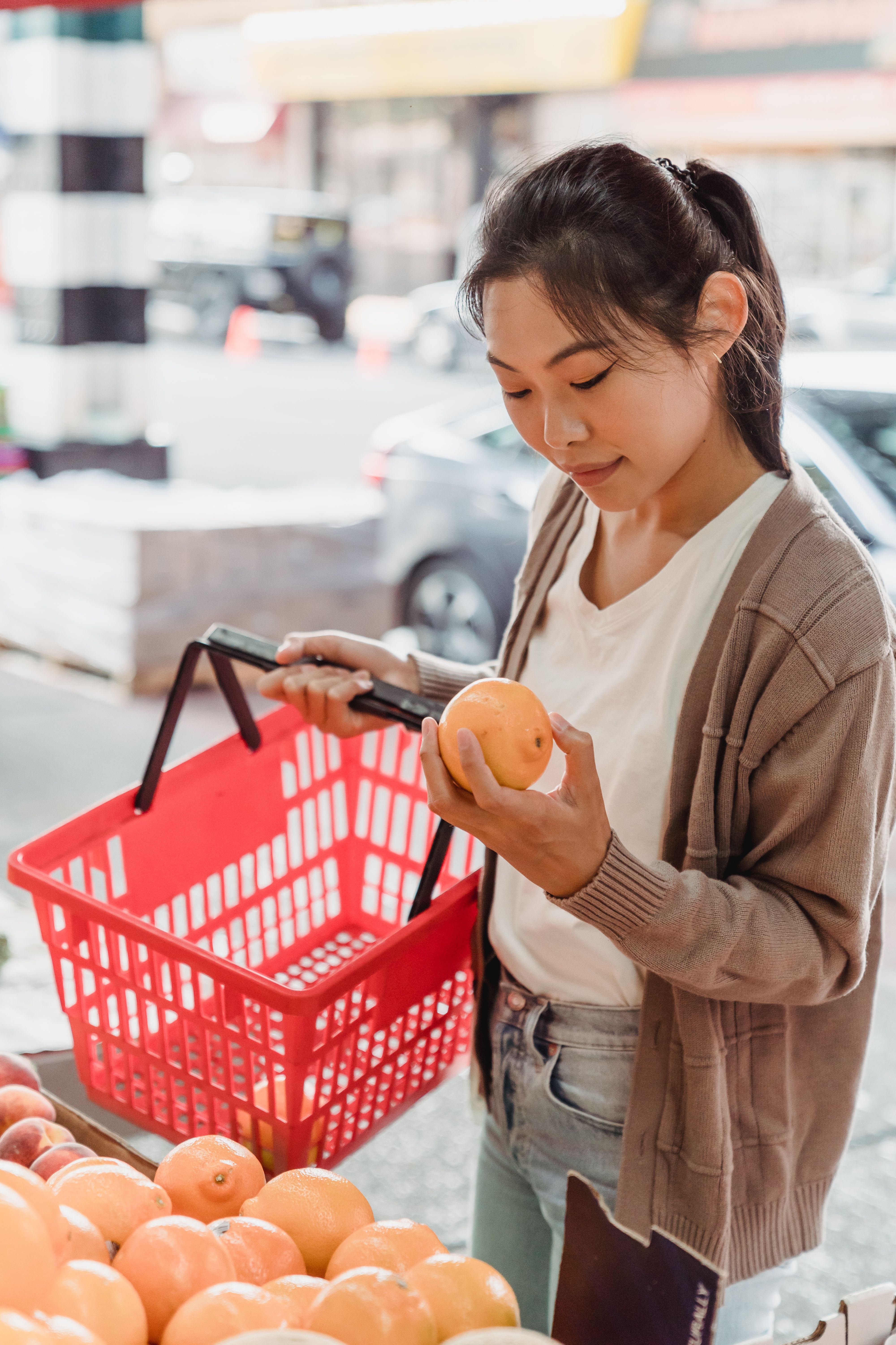 Young woman with a basket selecting fruits at an outdoor market.
