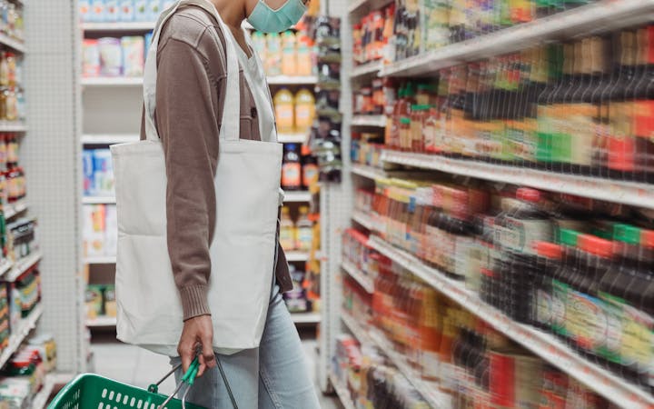 Woman in face mask shopping for condiments during Covid-19 pandemic. New normal lifestyle.