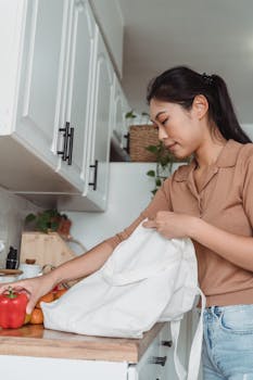 A young woman unpacks groceries on a kitchen counter, featuring peppers and a tote bag.