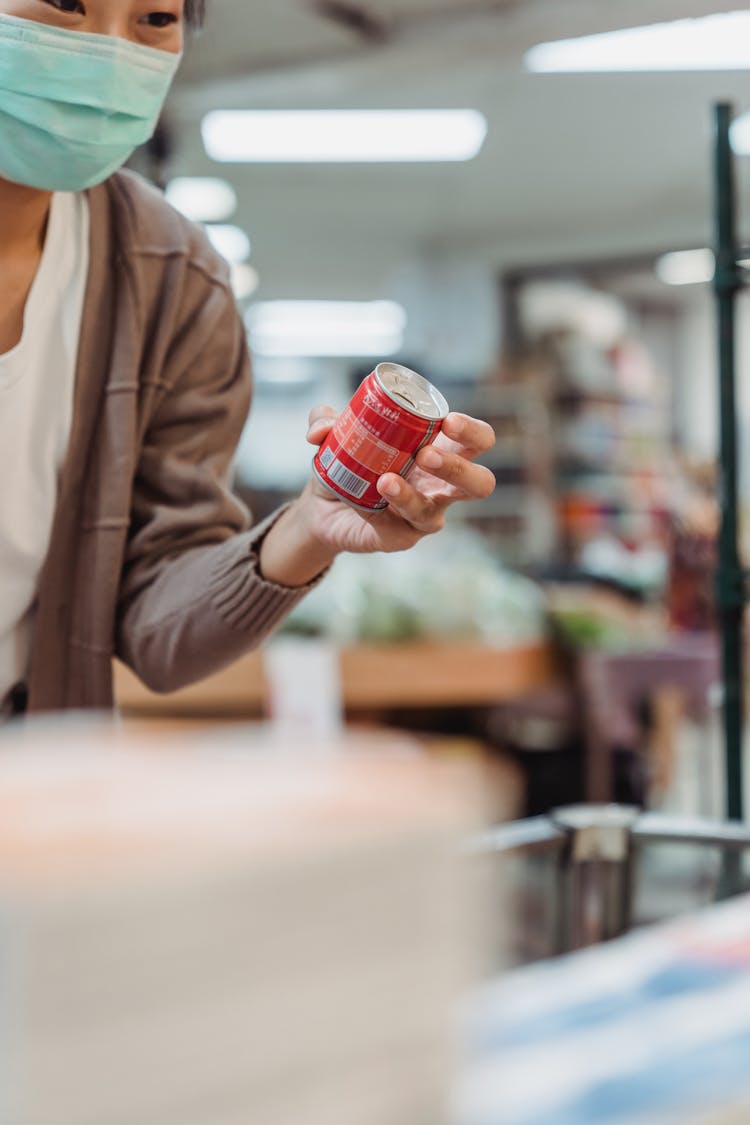 A Woman Wearing A Face Mask Holding A Canned Drink