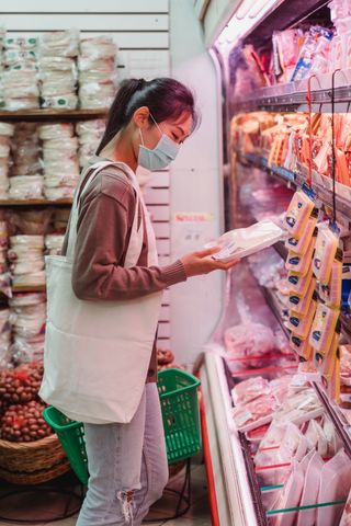 A young woman wearing a mask shops for packaged food at a grocery store.