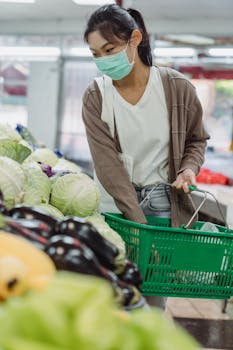 Asian woman wearing mask shopping for fresh vegetables in a supermarket.