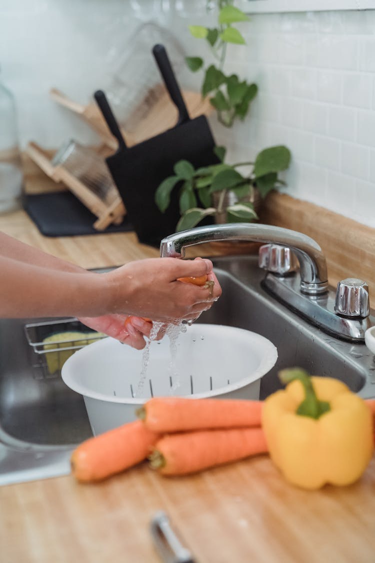 A Person Washing Vegetables On The Sink