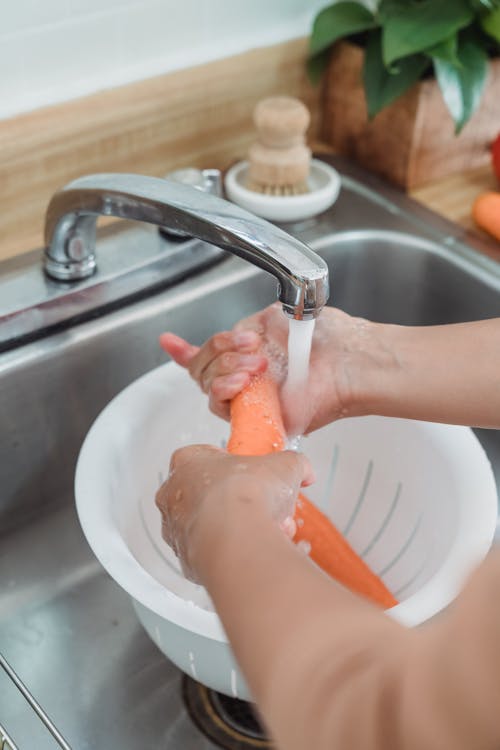 Free Person Washing Carrots in Kitchen Sink Stock Photo