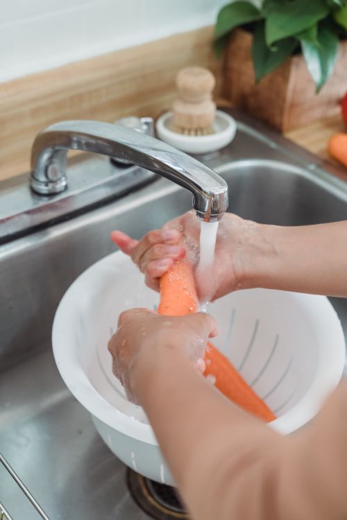 Free Hands washing fresh carrots under running water in a kitchen sink. Stock Photo