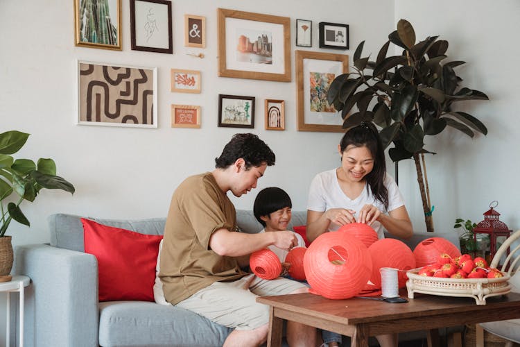 Family In An Interior With Pictures On A Wall Preparing Red Lantern Decoration