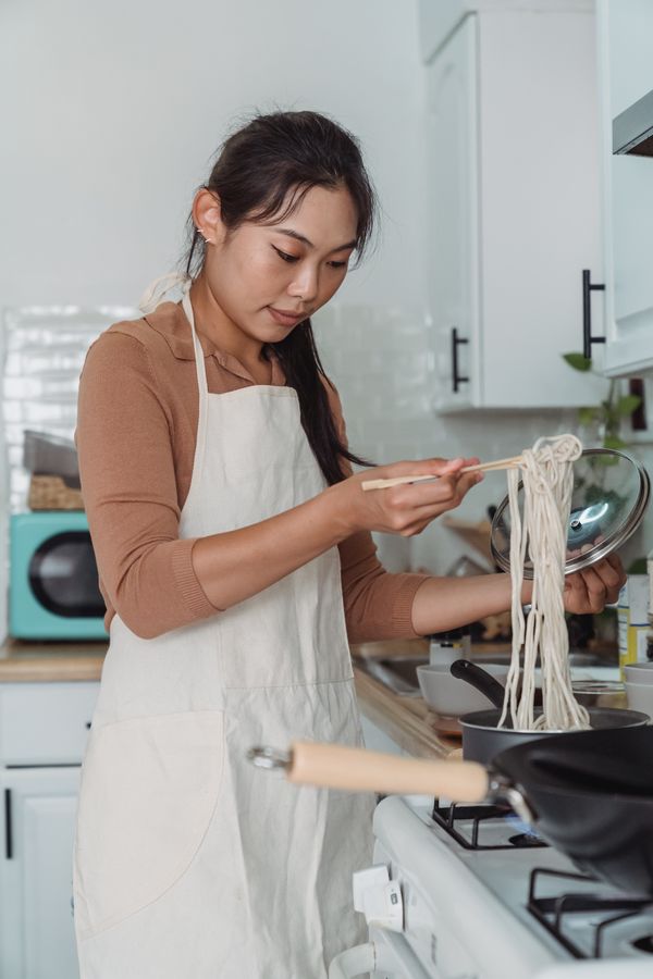 Hands lifting noodles from a bowl in a dim kitchen — photo by Kevin Malik on Pexels