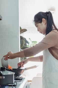 An Asian woman prepares a meal in a bright, modern kitchen. Indoor setting with a focus on home cooking.