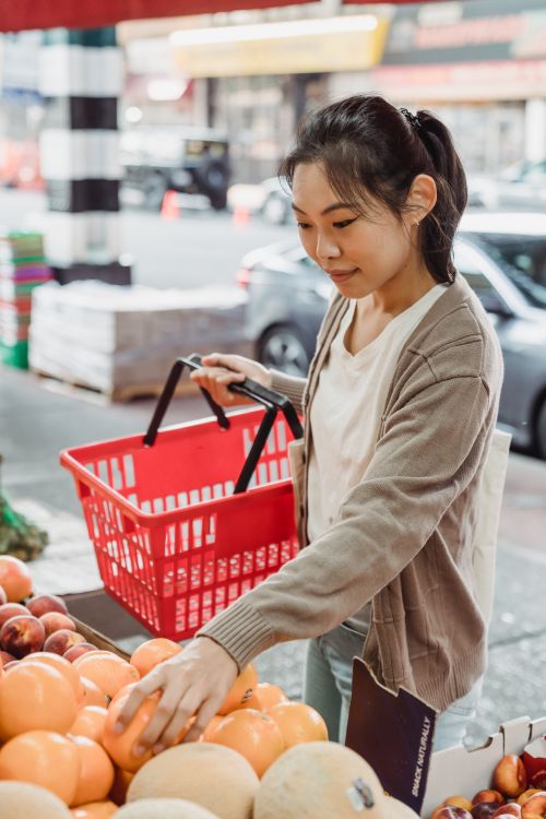 Free A young woman selecting fresh fruits at an outdoor market with a cheerful expression. Stock Photo