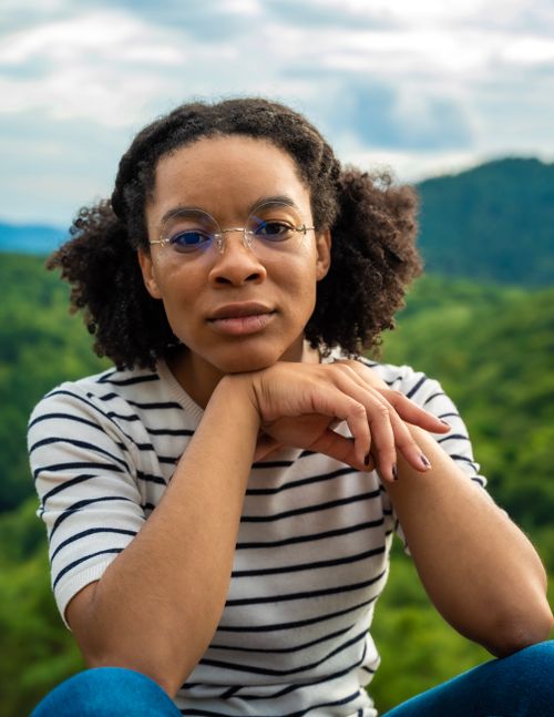Free Portrait of a young woman with eyeglasses sitting outdoors in a natural setting. Stock Photo