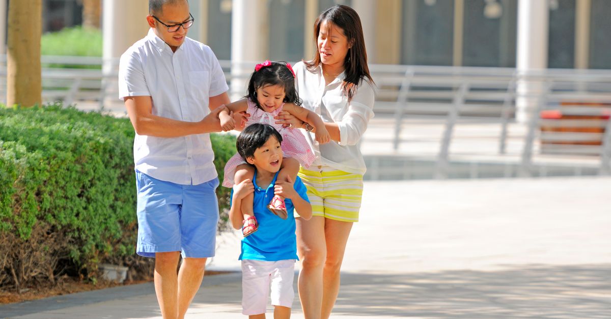A cheerful family enjoying a sunny walk in the park with playful piggyback rides.