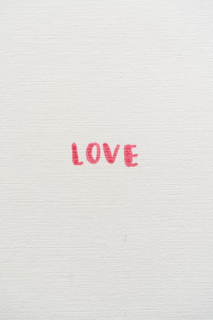 Simple minimalist art featuring the word 'Love' in red text on a textured white background.