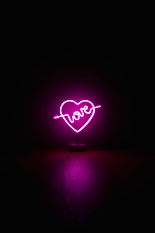 Free A pink neon heart sign with the word 'love' glowing on a black background. Stock Photo