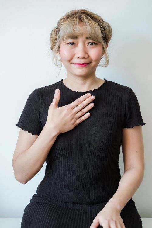 Free Portrait of a smiling woman in a black shirt with a hand gesture against a white background. Stock Photo