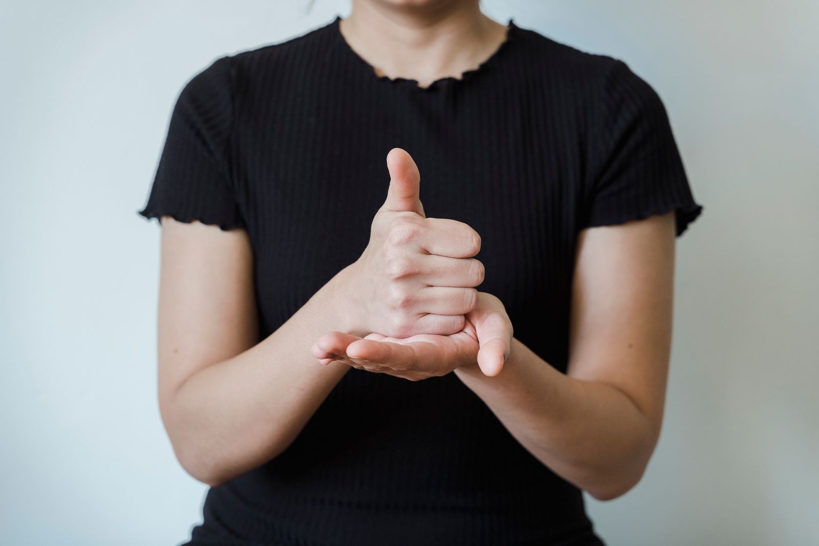 Person holding their wrist and thumb area while seated in bright natural light