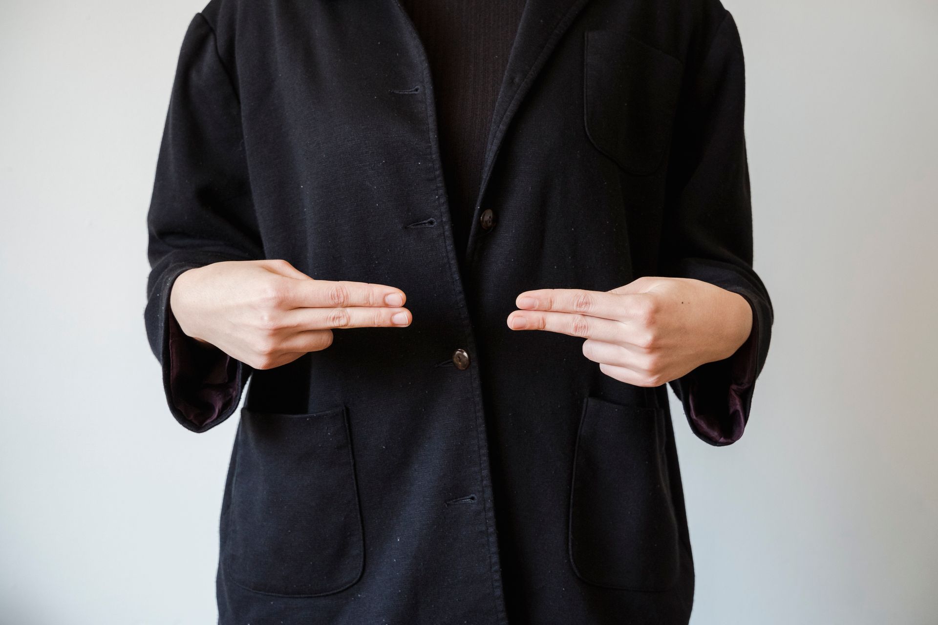 A close-up of a person making a hand sign gesture while wearing a black jacket.