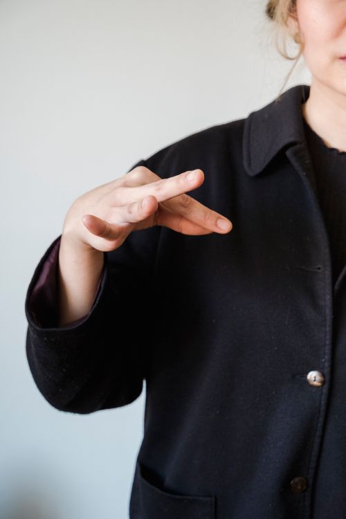Free A close-up image showing a woman in a black coat using sign language, indoors. Stock Photo