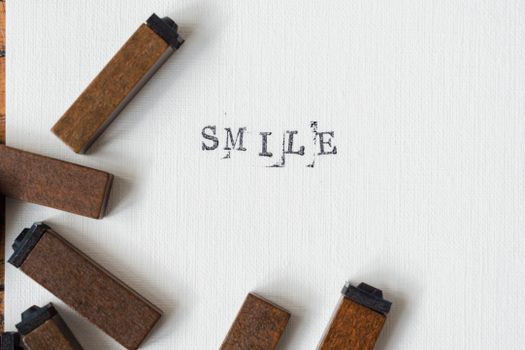 Artistic arrangement of wooden letter stamps spelling 'SMILE' on textured paper.