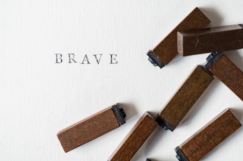 Close-up of Ink Letter Stamps and the Word Brave Written on Paper