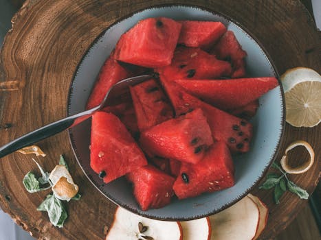 Sliced watermelon in a bowl on a wooden board with citrus and apple accents.