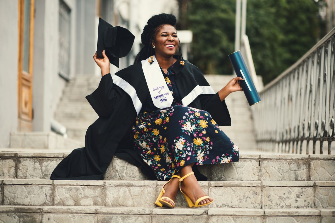 woman joyfully celebrates graduation sitting on stairs with diploma an