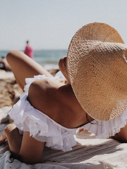 A Person in Beach Hat Wearing White Off Shoulder Top while Lying on a Blanket