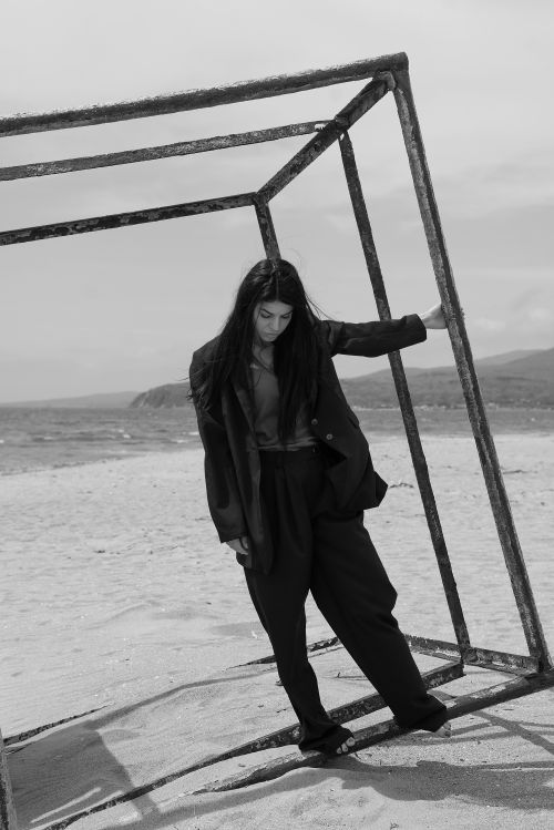 Free Stylish woman standing in a cubic frame on a sandy beach, capturing a moody black and white aesthetic. Stock Photo