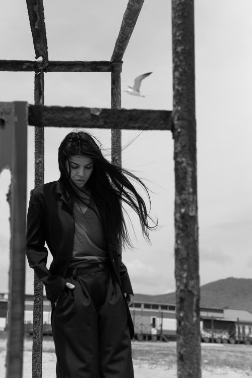 Free Woman in a windy coastal setting with industrial elements in black and white. Stock Photo