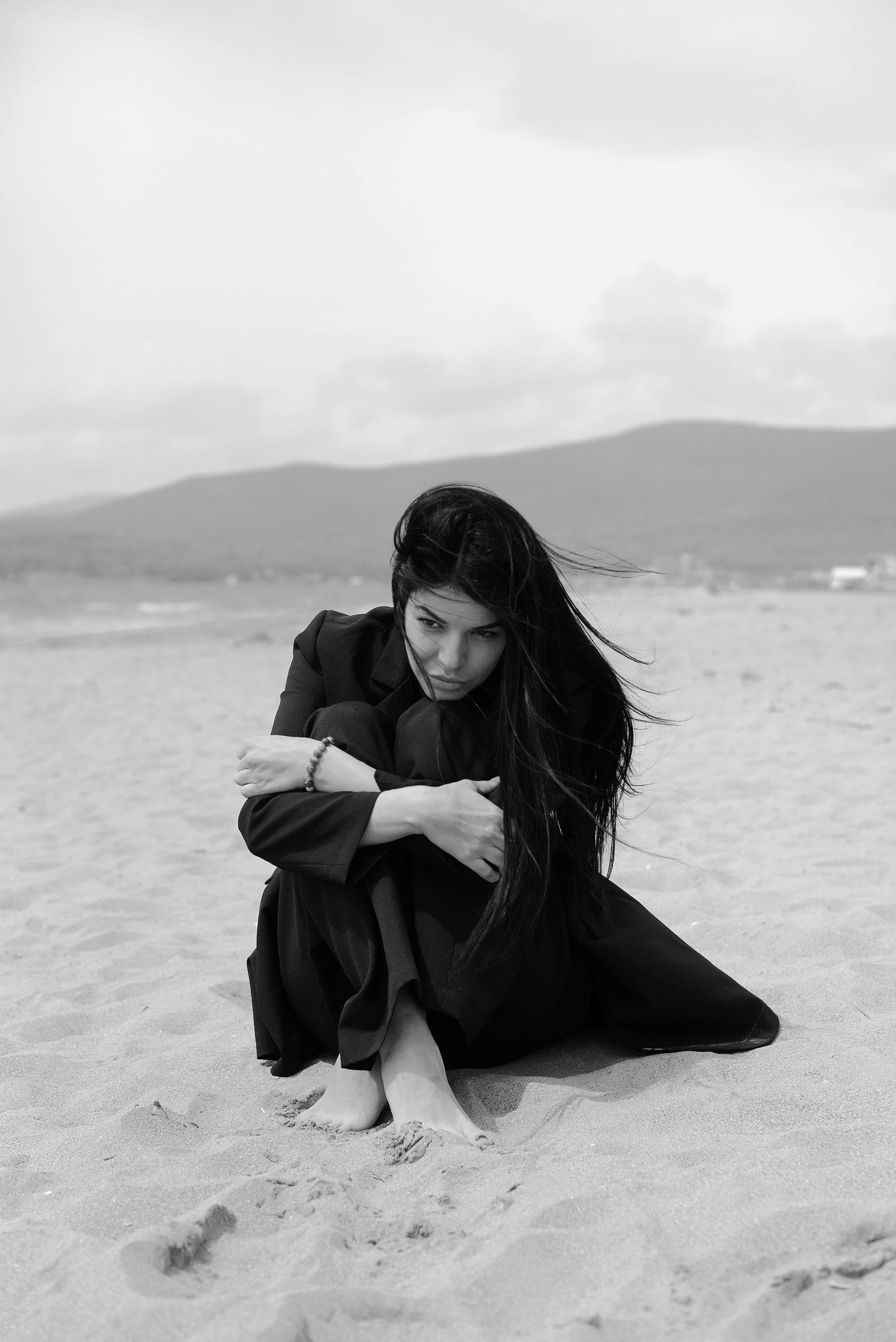 grayscale photo of a woman sitting on shore
