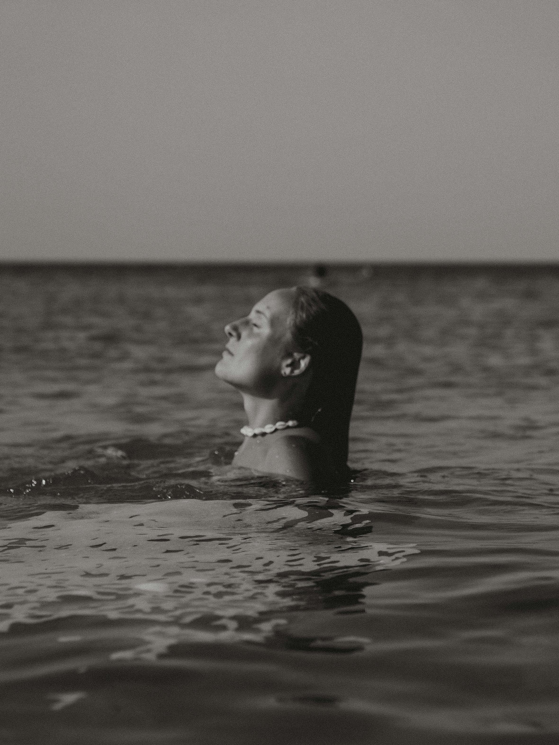 An artistic black and white photo of a woman relaxing in the ocean, exuding calmness.