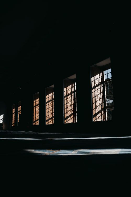 Free A moody shot of light filtering through large industrial windows, casting shadows indoors. Stock Photo