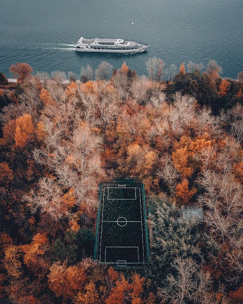 Free Drone Shot of a Basketball Court Near the Sea with White Ferry Sailing Stock Photo