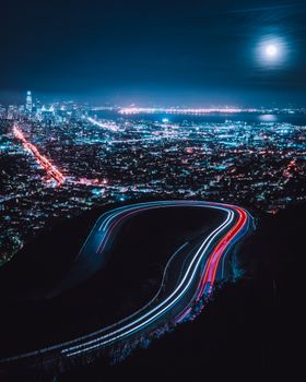 Long exposure capturing San Francisco's city lights and road paths under a full moon.